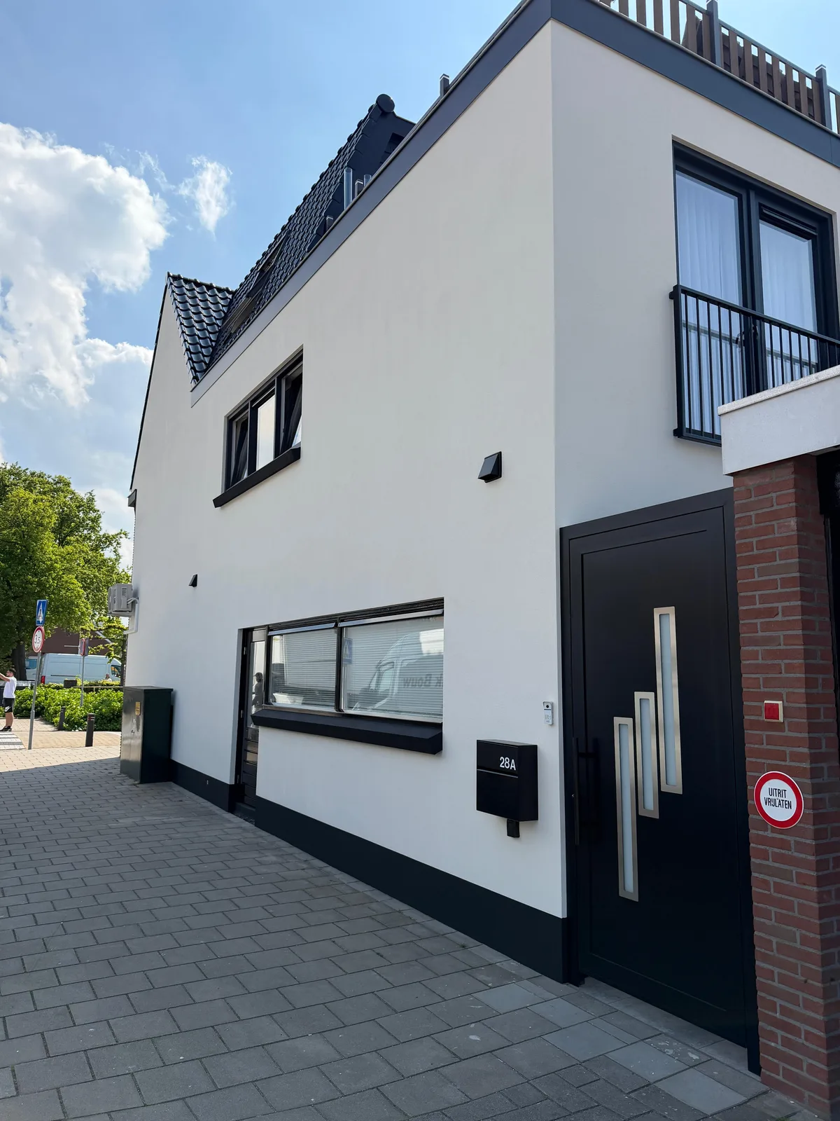 Wit gestuukte woning met zwarte kozijnen, een garage en een balkon, naast een bakstenen zijgevel