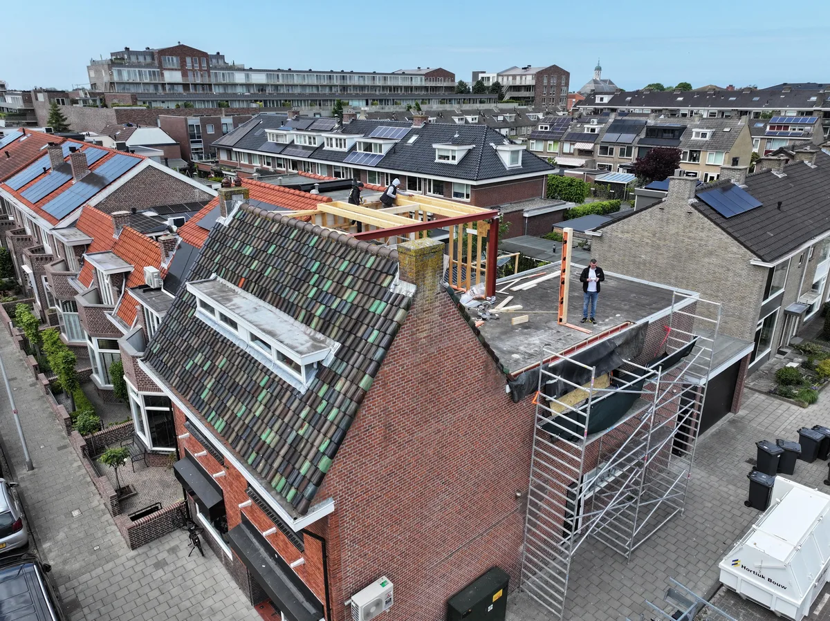 Luchtfoto van de woning tijdens de verbouwing, met steigers rond de gevel en het oude dak