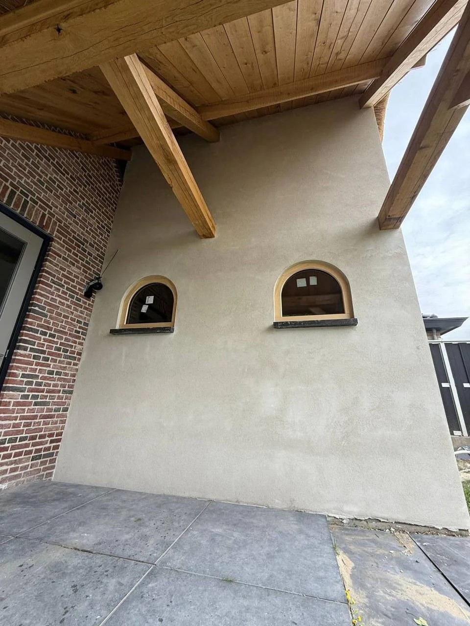 Gestuukte wand met twee boogramen onder een houten overkapping