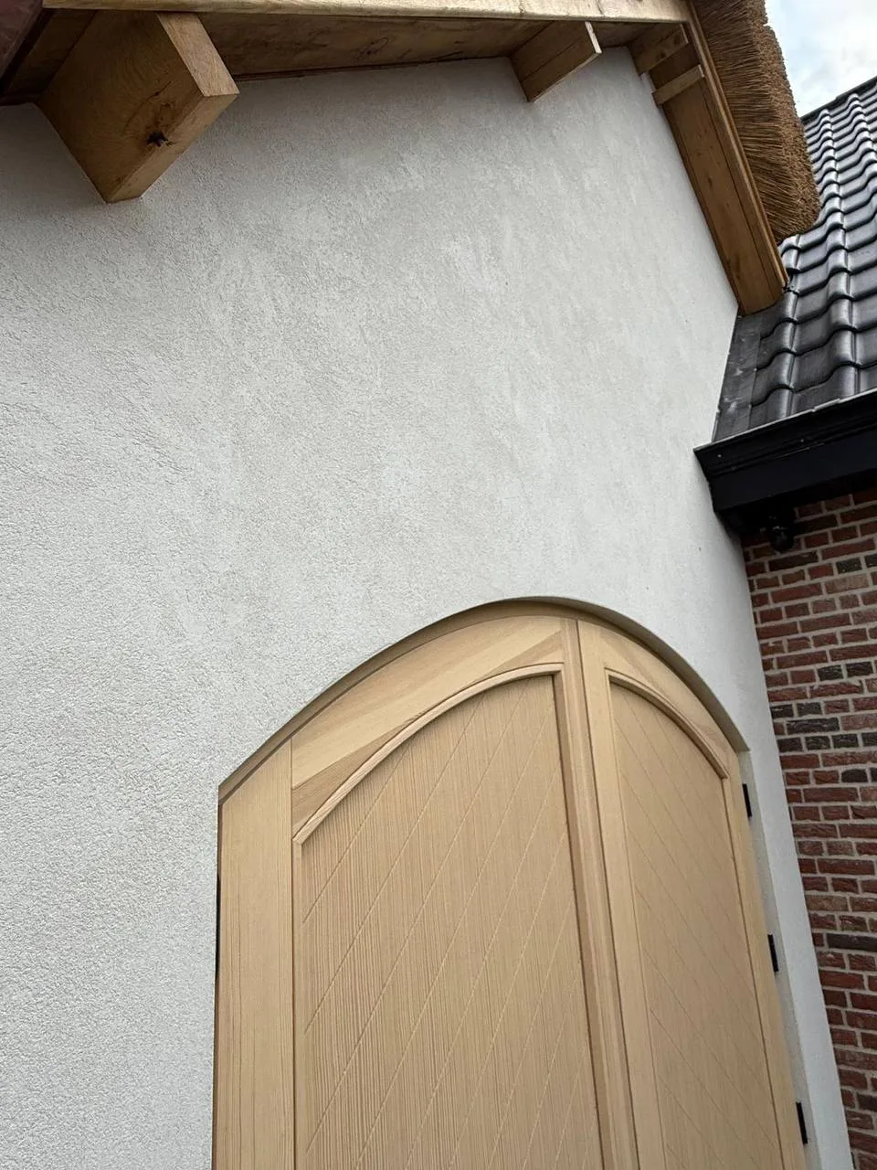 Gestuukte gevel die strak doorloopt tot tegen de houten boogdeur