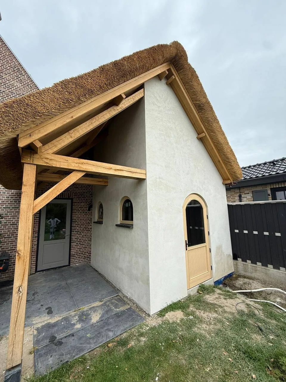 Gestuukt bijgebouw met een rieten dak, een houten overkapping en een boogdeur