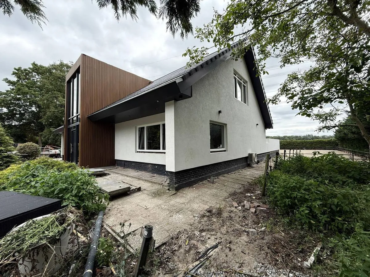 Woning met een witte gestuukte gevel naast een hoge houten gevelbekleding