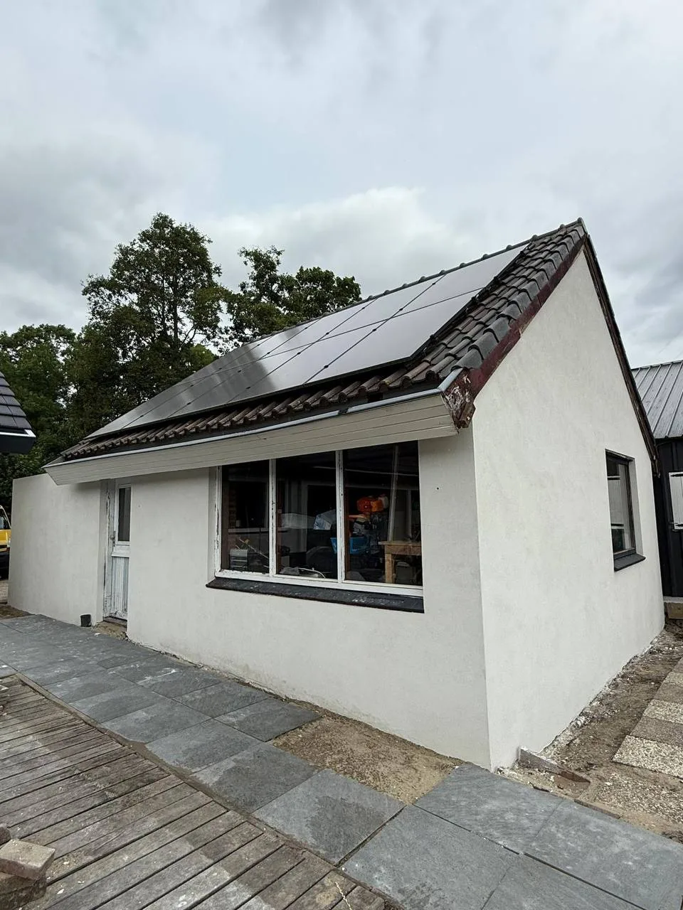 Wit gestuukte woning met zonnepanelen op het dak en een grijze plint