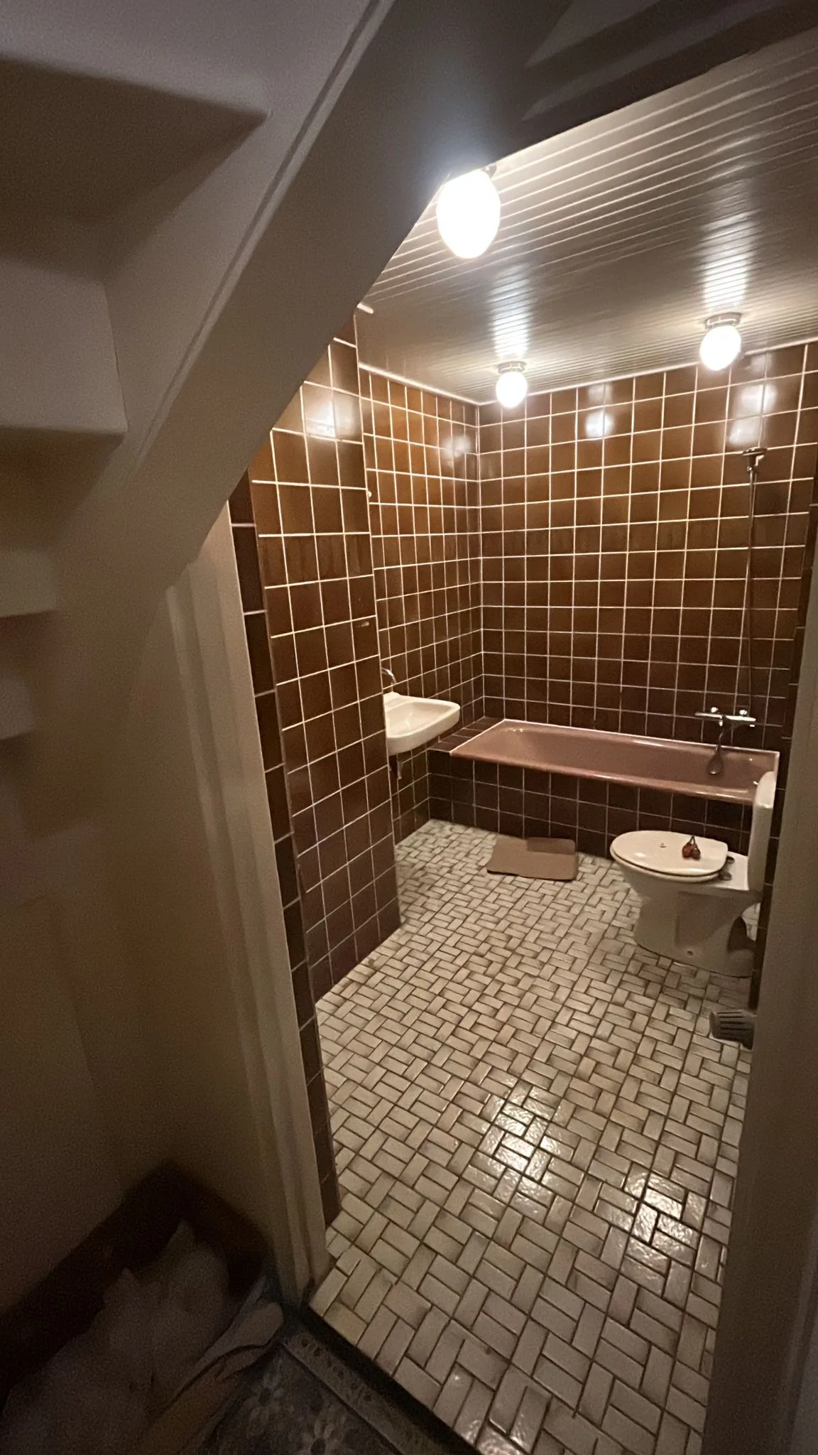 Badkamer voor de verbouwing: bruin wandtegelwerk en een ingebouwd bad