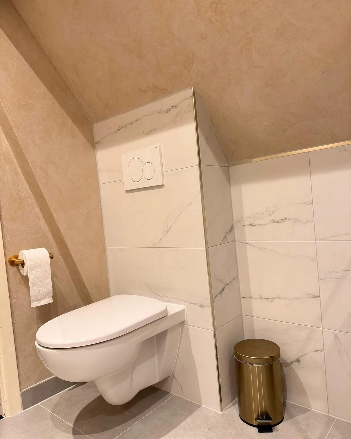 Hangtoilet tegen een wand van marmerlooktegels, met een pedaalemmer ernaast