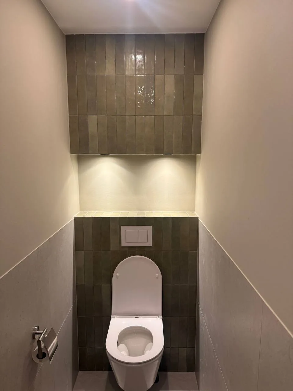 Toilet met een hangtoilet en een wand in donkere tegels achter de spoelknop