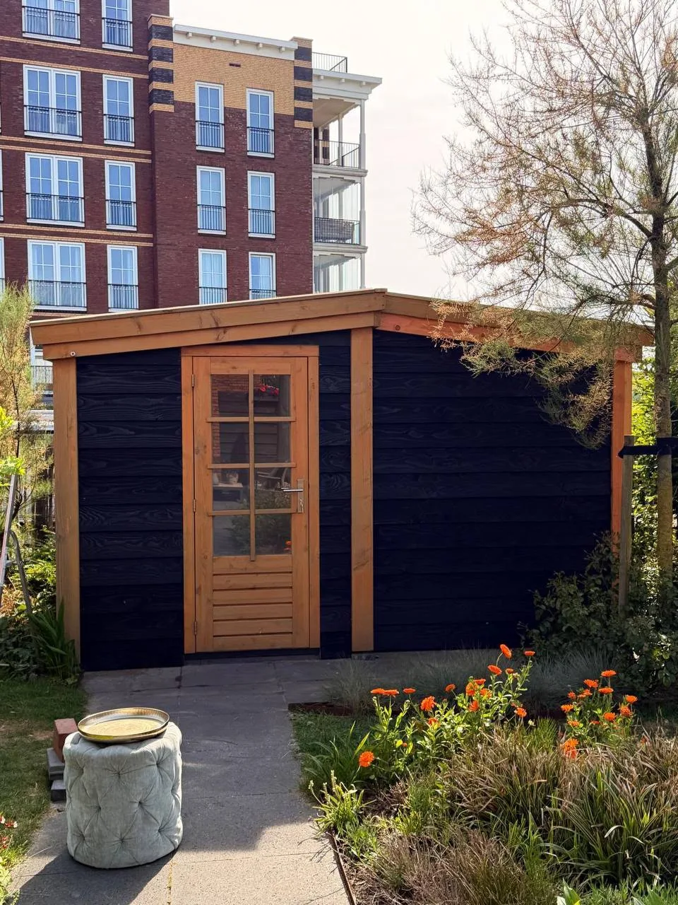 Zwarte houten berging met een naturel eiken deur en kozijn, in een tuin