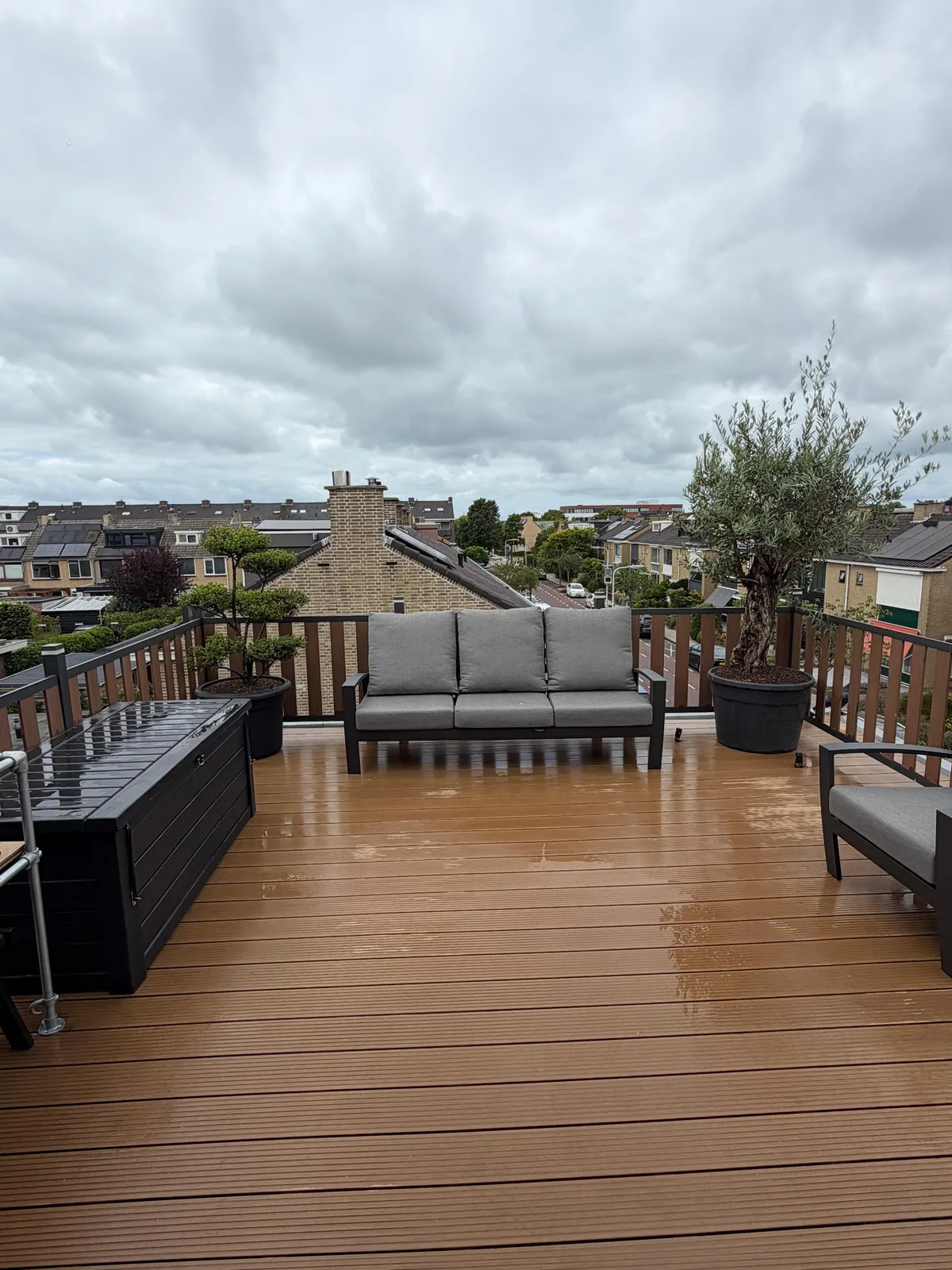 Dakterras met houten vlonder, loungebank en plantenbakken, met uitzicht over de daken