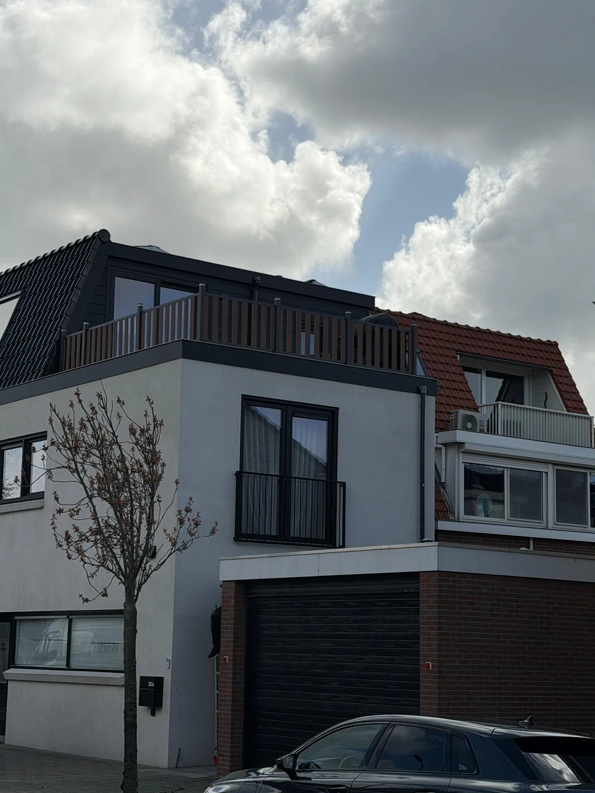 Zijgevel van de woning met zwarte kozijnen en het balkon van de opbouw